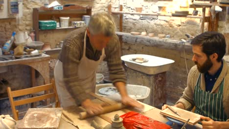 potter teaching his colleague to roll the clay