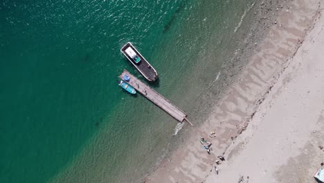 Fisherman-departs-with-sailing-boat-at-japanese-blue-sea-coastline-aerial-drone-top-down-view-of-summer-in-wakayama-Japan-traveling-destination,-revealing-shot-of-town-and-mountain-background