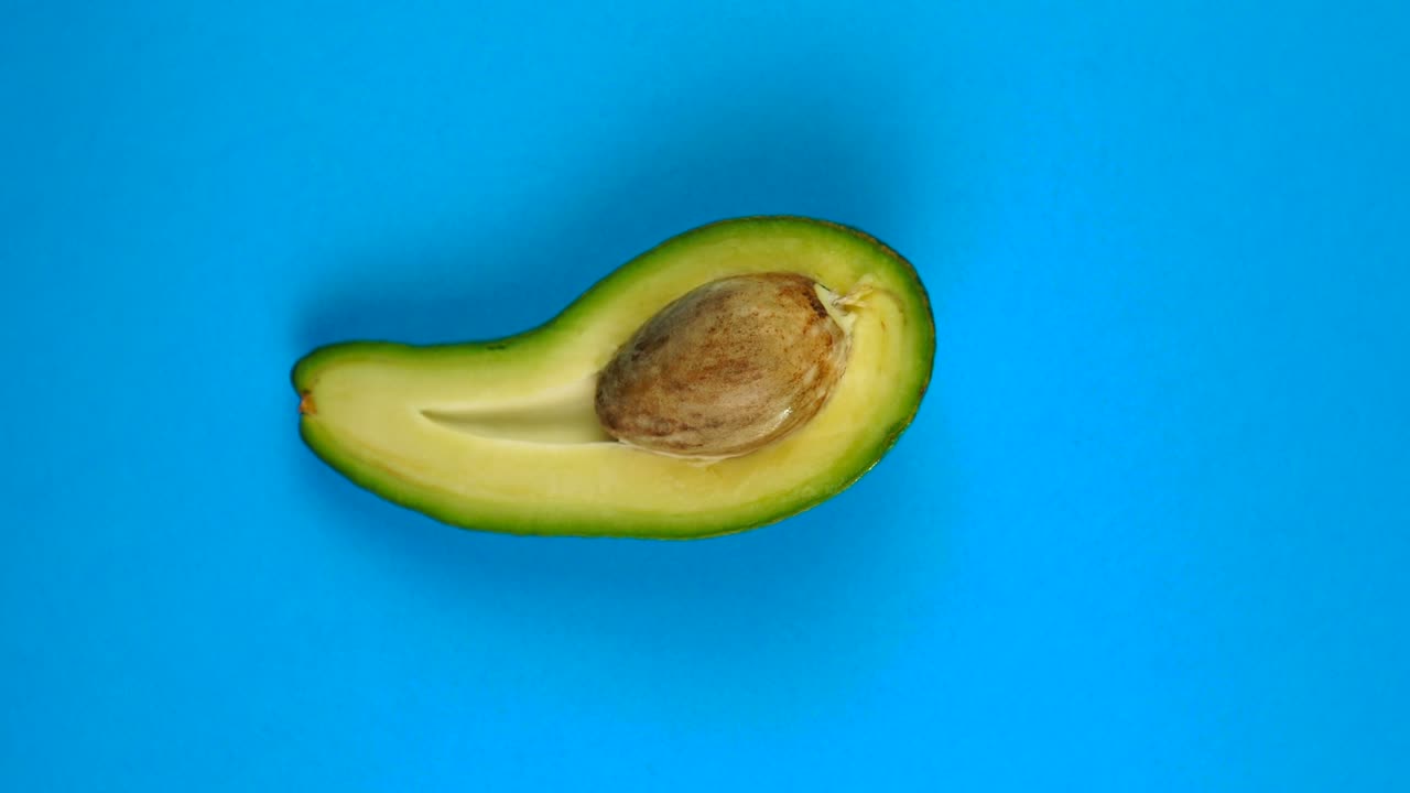 Mezzo frutto di avocado che ruota velocemente su un tavolo blu. L'avocado è un frutto altamente nutriente.