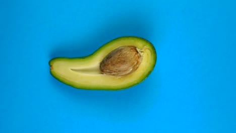 la mitad de la fruta del aguacate girando rápidamente en la mesa azul. el aguacate es una fruta muy nutritiva.