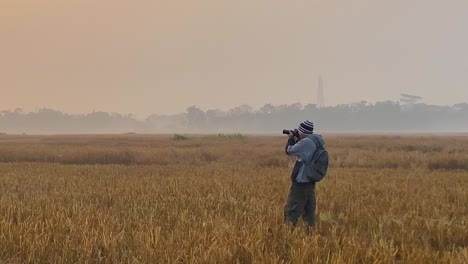 single photographer wearing winter clothing and backpack takes pictures of field