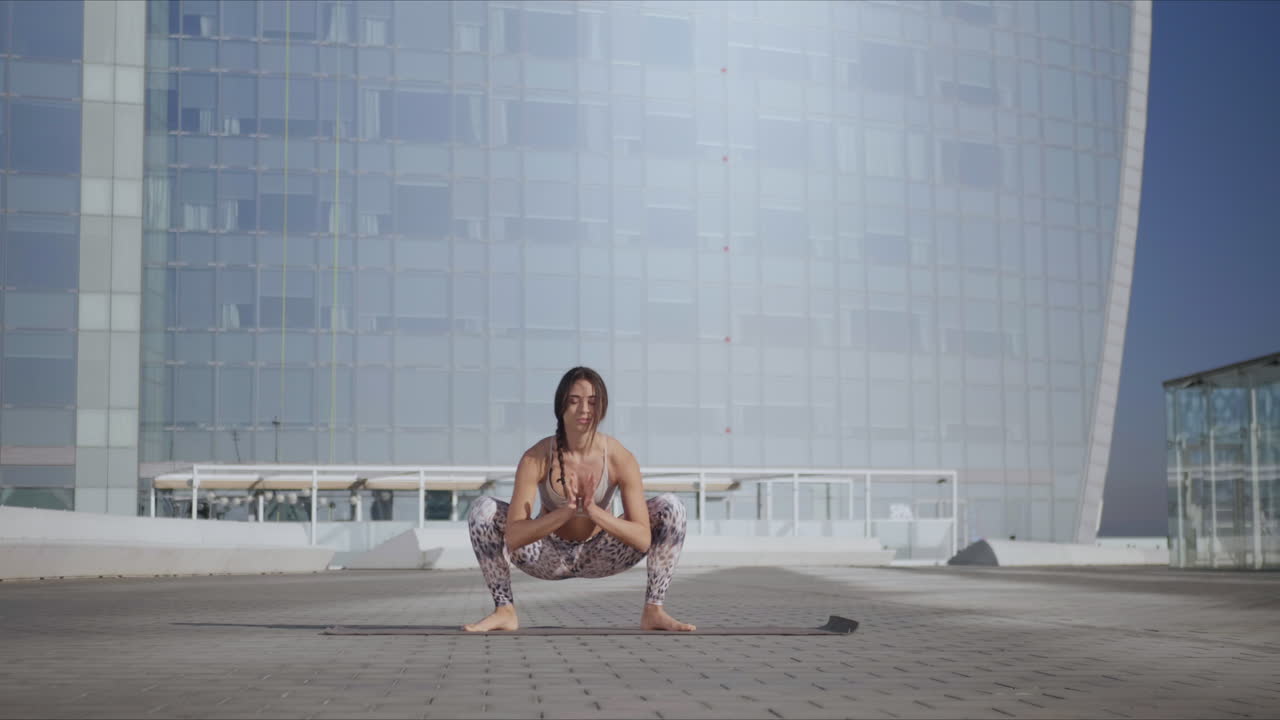 Woman performing yoga in urban street. Lady doing garland pose on mat outdoors