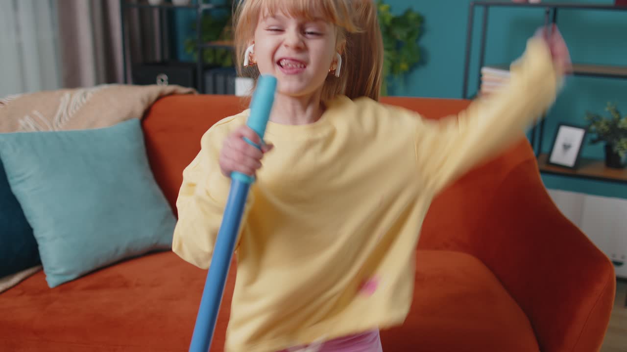 Funny toddler girl kid cleaning washes floors with a mop at home dancing singing in positive mood
