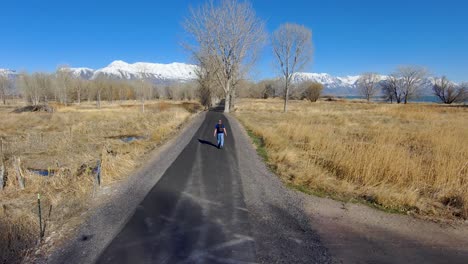 mature, balding man walking with a backpack down a nature trail with the snow-capped mountains in the distance - tilting aerial view