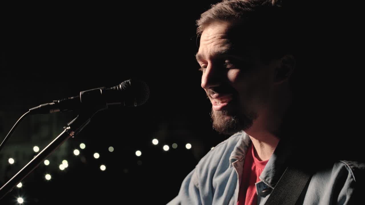 un músico está tocando la guitarra en un gran escenario con miembros de la audiencia sosteniendo linternas en el fondo. el auditorio está lleno de hermosas luces parpadeantes.