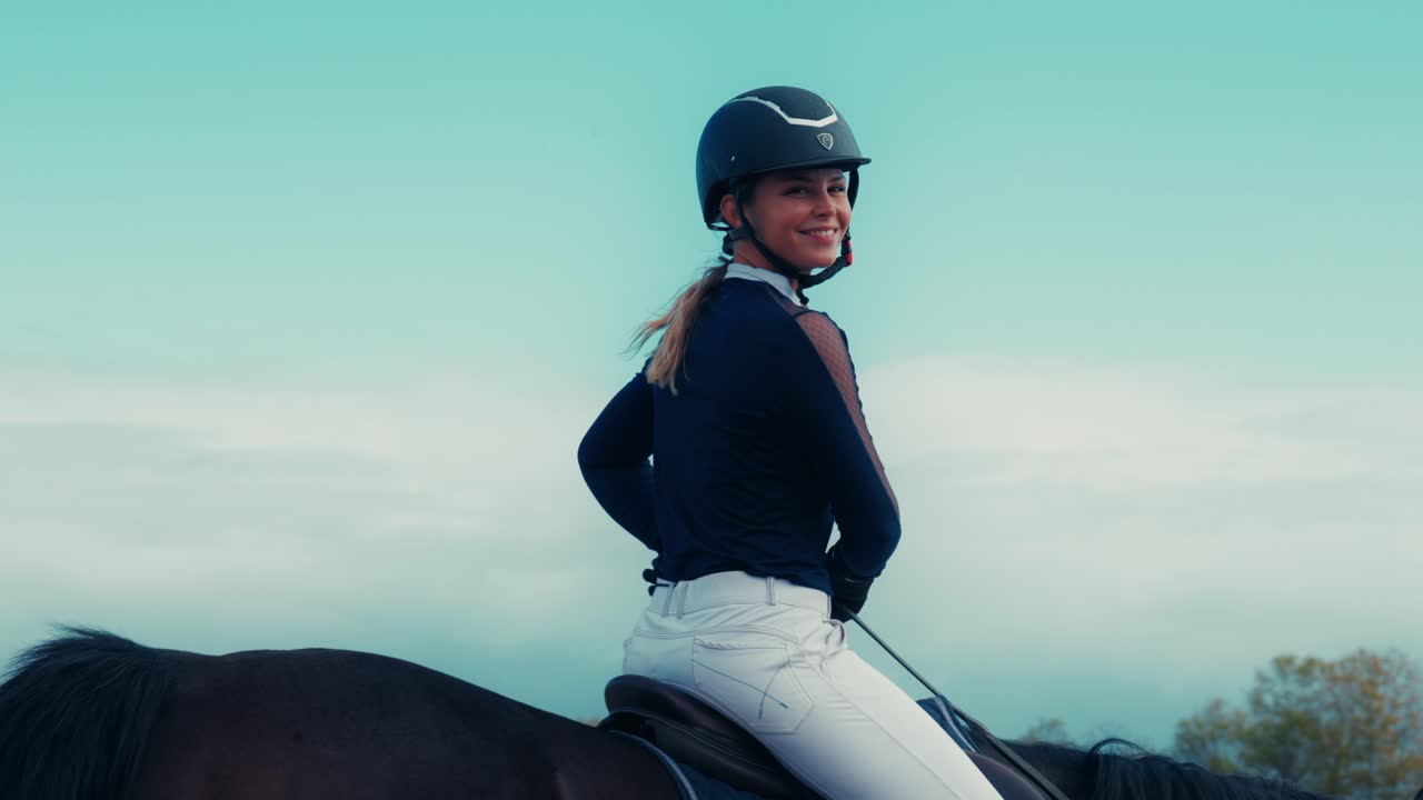 Young female equestrian rider smiles while riding a horse during training. Natural outdoor scene showing confidence, sport lifestyle, and horseback riding practice