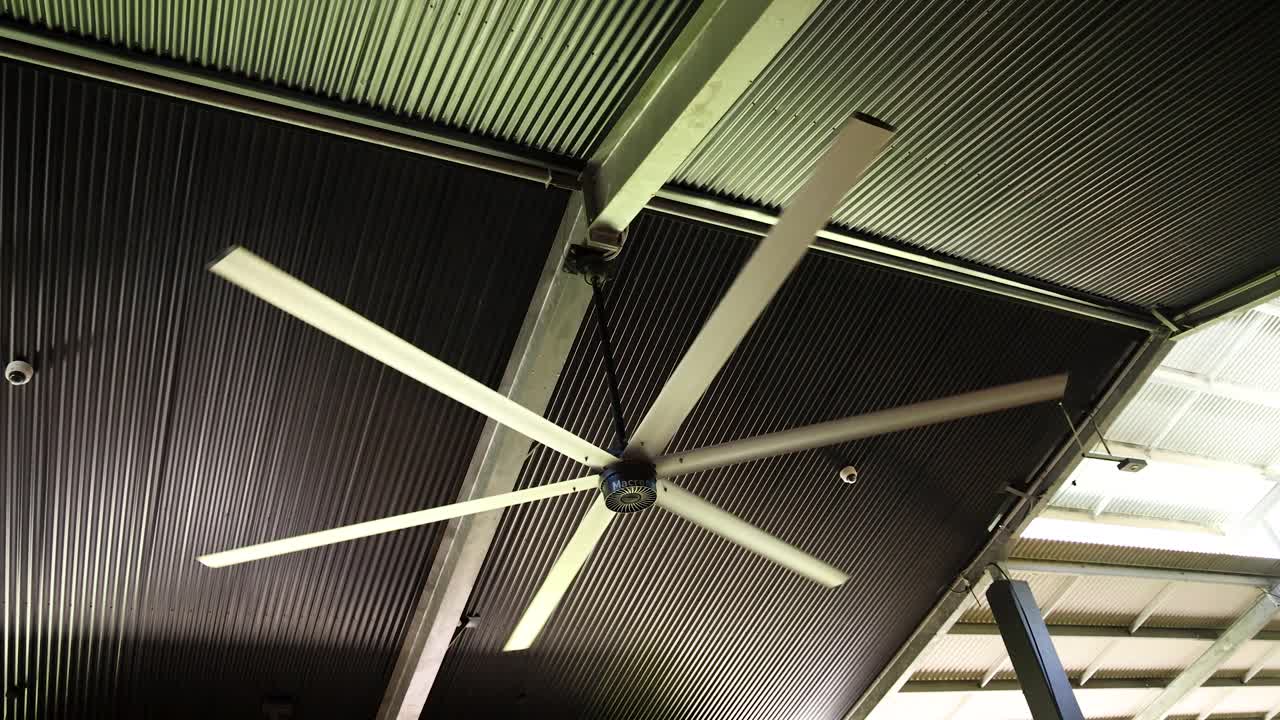 A low angle shot shows a large industrial fan spinning against a corrugated metal ceiling