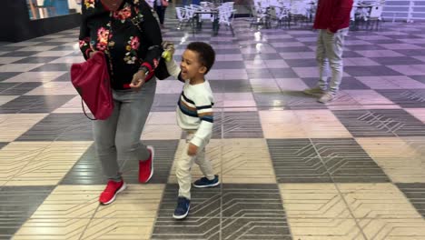 playful black child 3-year-old playing to chase his mother with a dinosaur in his hand outdoor