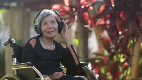 asian senior woman listening music with headphone in backyard.