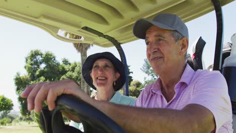 Kaukasisches-älteres-Paar,-Das-Auf-Dem-Golfplatz-Einen-Golfwagen-Mit-Schlägern-Auf-Der-Rückseite-Fährt