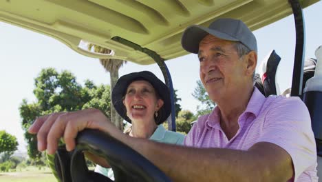 caucasian senior couple driving a golf cart with clubs on the back at golf course