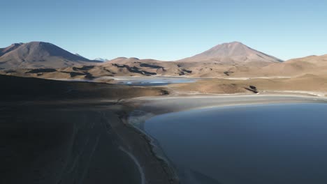 Laguna-Route-Bolivia,-Aerial-Drone-Above-Blue-Lagoon-and-Dunes-Sandy-Terrain,-South-America-Travel-and-Tourism,-Shore-and-Rock-Formations