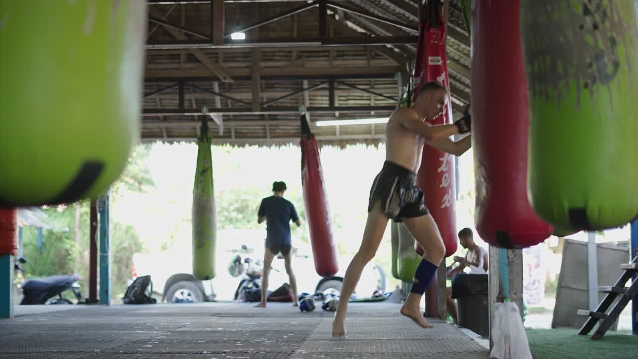 Man training Muay Thai with punching bags at a gym