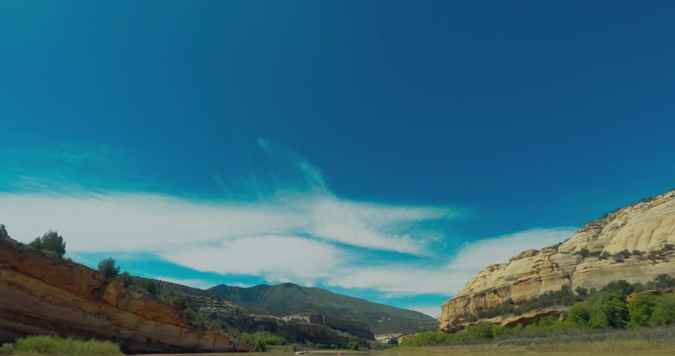 Ampia valle di canyon sotto nuvole drammatiche e montagne desertiche a strati, sfondo sereno e aperto