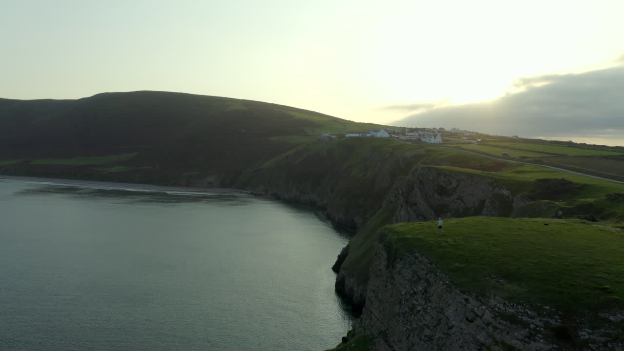 imágenes de drones de una persona caminando hacia el borde del acantilado en la bahía de rhossili en gower, gales del sur