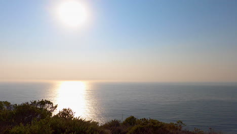 Slow-zoom-out-of-the-sun-beginning-to-set-over-the-Pacific-Ocean-along-the-Northern-California-Cliffside-on-a-warm-summer-afternoon---4K