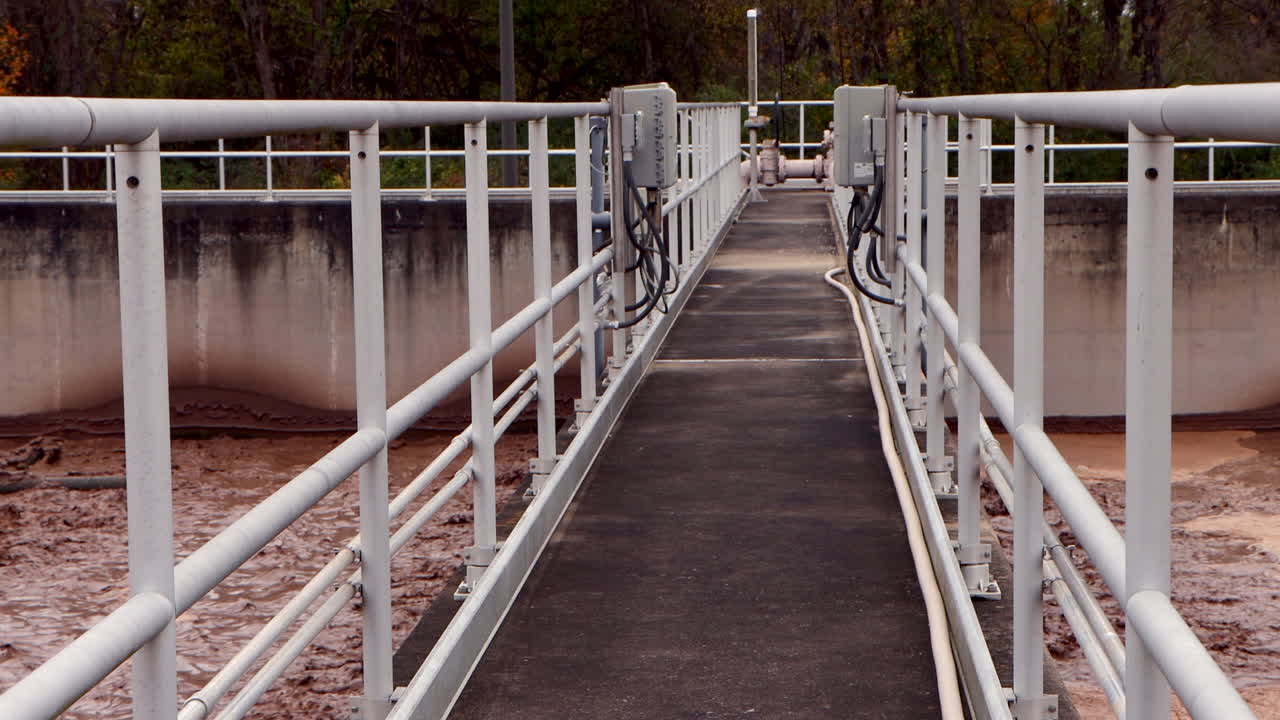 A chocolate-colored sewage bath churns below the center walkway of a wastewater treatment plant, showcasing the industrial flow and dynamic treatment process