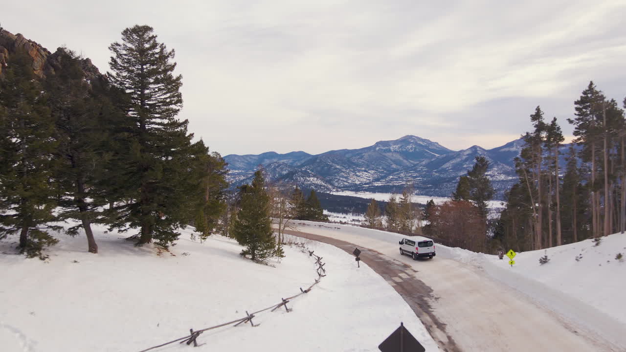 Drone Shot a Car drives in the snow at the Rocky Mountain Park pass drive with Deer Mountain in the background. Aerial Shot van drive at Many Parks Curve Overlook. Winter driving in Colorado