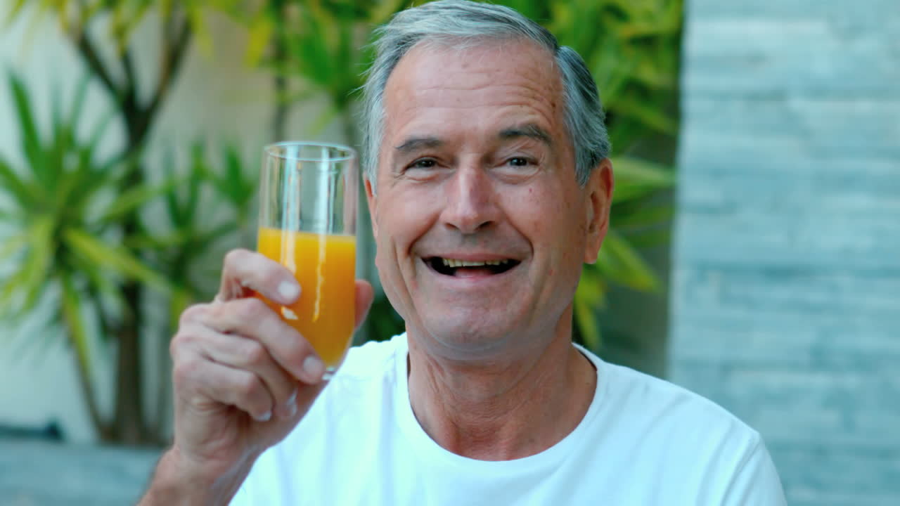 Hombre jubilado brindando con jugo de naranja al aire libre