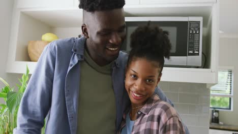 video of happy african american couple embracing in kitchen and looking at camera