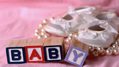 baby in letter blocks beside booties and pearls on pink blanket