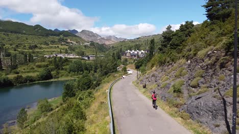 Sallent-de-Gallego-at-Tena-Valley,-Huesca,-Aragon,-Spanish-Pyrenees,-Spain---Aerial-Drone-View-of-a-Tourist-Girl-Mountainbiking-around-Lake-Embalse-de-Bubal