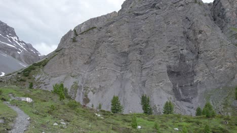 aerial drone footage panning through a glacial mountain landscape with patches of snow, isolated trees a remote alpine hiking trail in switzerland