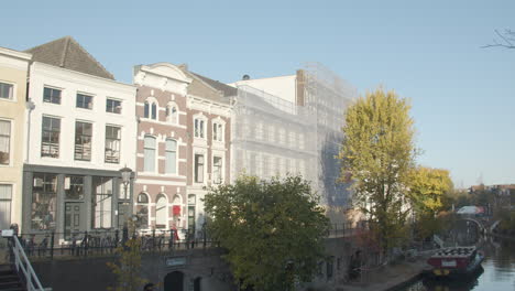 Woman-cycling-past-beautiful-old-buildings-near-canal-in-Utrecht,-the-Netherlands