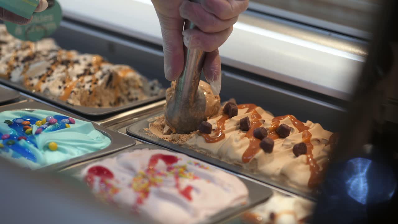 Un commesso che serve gelato al cioccolato e caramello in una vaschetta.