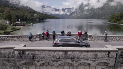 Video-Mit-Drohne-Der-Flugzeugentdeckung-Des-Krans,-Der-Im-Bohinjer-See-Aufsteigt,-Mit-Der-Brücke-Im-Vordergrund,-Vorbeifahrenden-Menschen-Und-Fahrzeugen