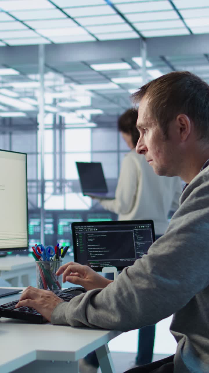 Vertikal video: IT-programmerer ankommer jobb i datasenter, sitter ved en PC-pult.