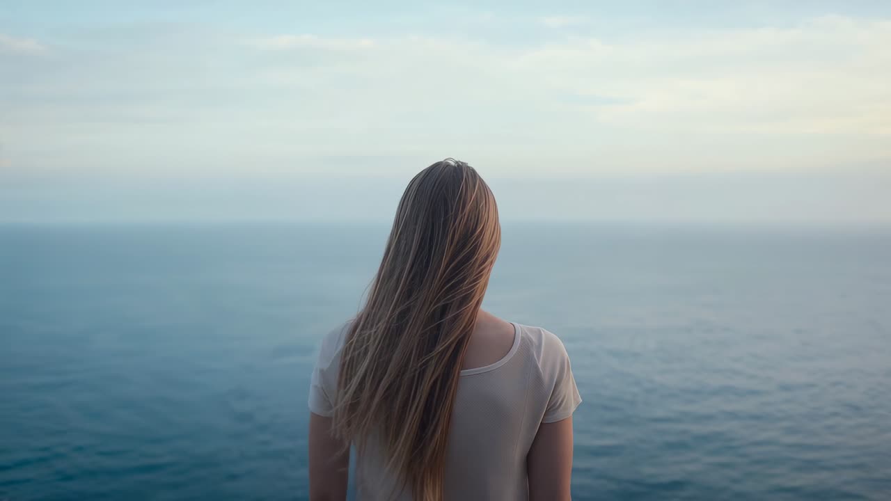 Feeling gentle breeze picking up, lone woman lifting hair while scanning ocean horizon from cliff