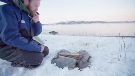 man blowing firewoods surrounded with rocks - making campfire