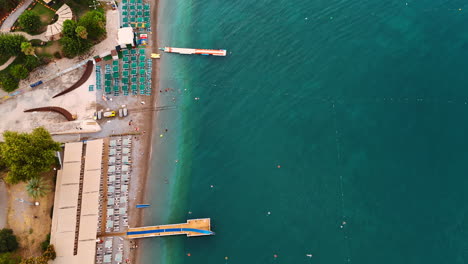 tranquil coastal beach views. clear turquoise waters meet sandy shores lined with sunbeds and a wooden pier under a sunny sky