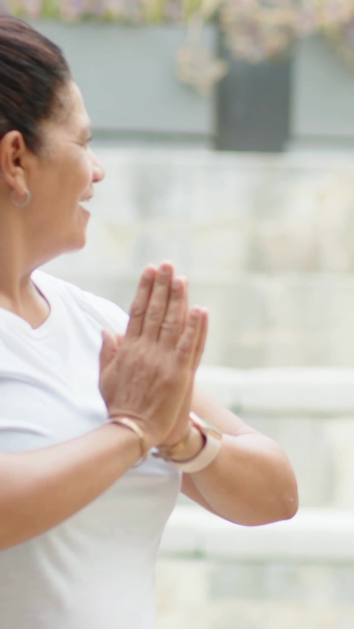 Video verticale: Donna che inizia con le mani vicino al petto, premendo i palmi per la calma sul patio, con fascia e spazio per il testo.