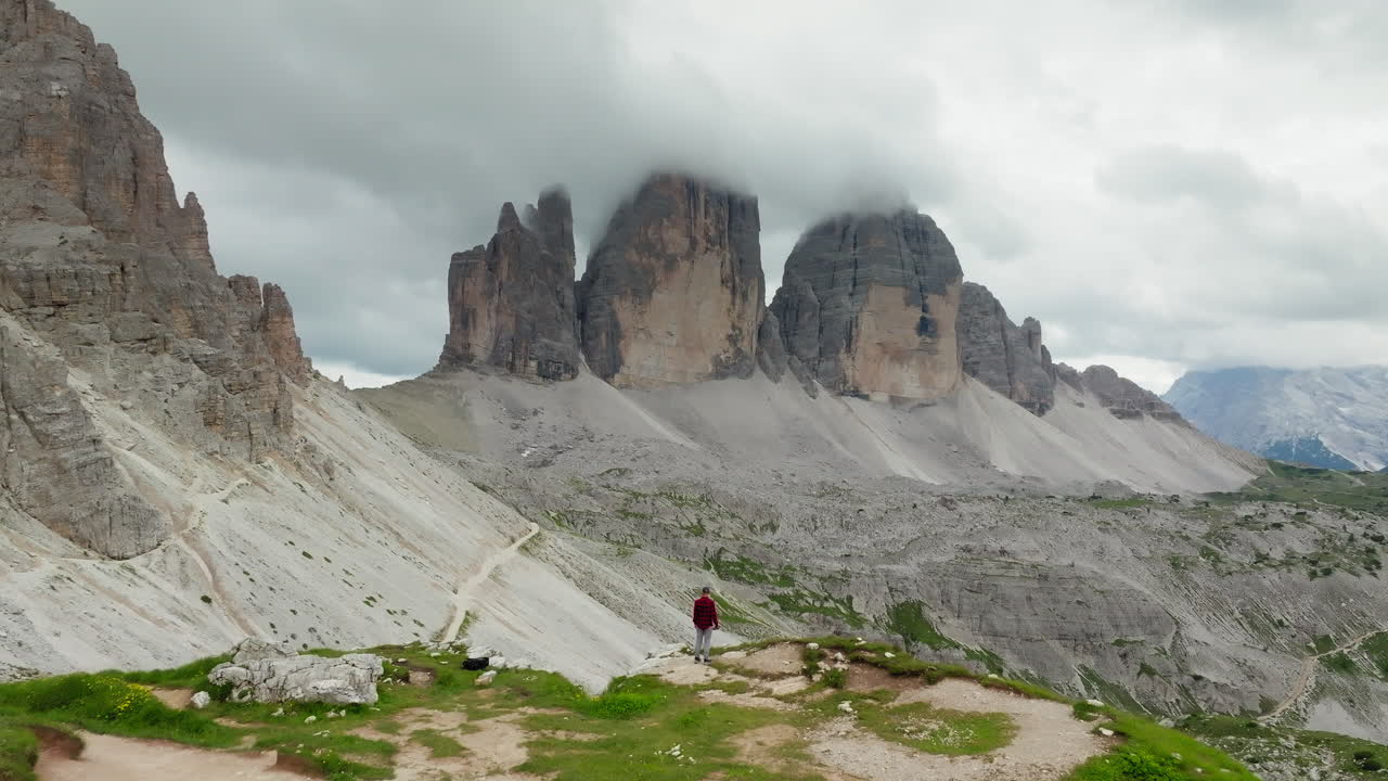 Scenic aerial approach of adventurer admiring Tre Cime di Lavaredo with rocky peaks and lush slopes in Dolomites