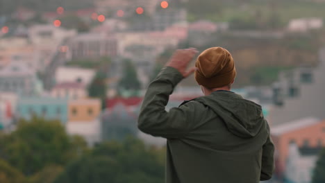 young caucasian man drinking alcohol on rooftop dancing enjoying cold refreshing beer looking at city skyline