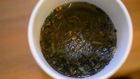 close -up from the top of green cup of tea in preparation with steeping leaves