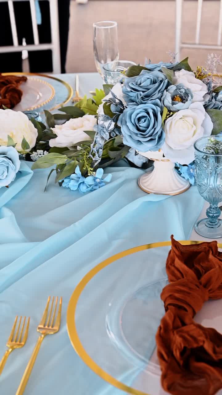 Elegant wedding table decor with blue runner and gold. Detailed view of formal table setting featuring blue glassware gold cutlery and white floral centerpieces