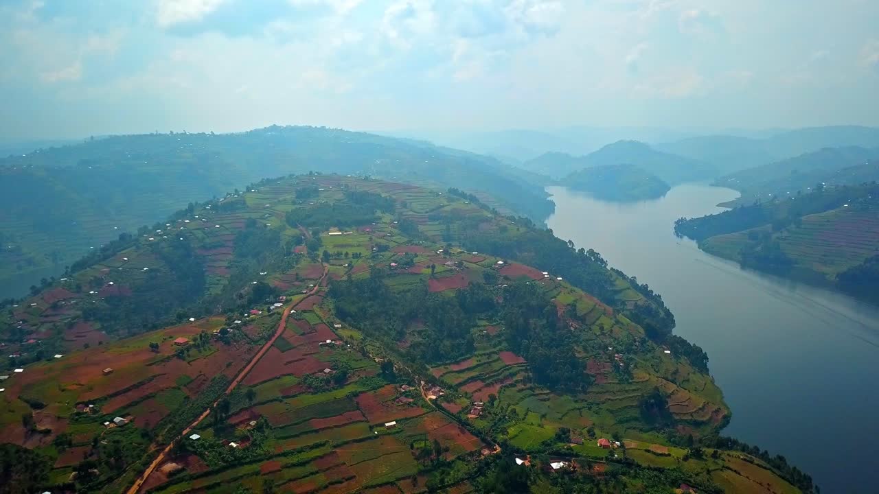Suggestiva ripresa aerea in discesa su rigogliose colline terrazzate e case sparse vicino al Lago Bunyonyi, Uganda, che mostra paesaggi rurali, strade tortuose e tranquilli bracci d'acqua che si snodano tra gli altipiani