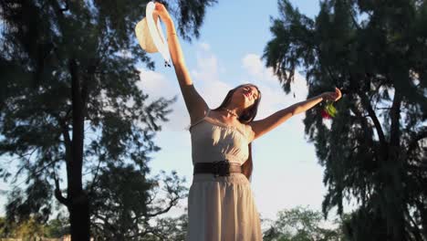 Hermosa-Joven-Feliz-Y-Libre-Levantando-Los-Brazos-Con-Sombrero-Y-Rosa-En-La-Naturaleza-Al-Atardecer