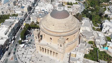 a far view, aerial 4k drone, footage tilt revealing the mosta rotunda dome, a roman catholic church, and the surrounding city blocks of malta near it