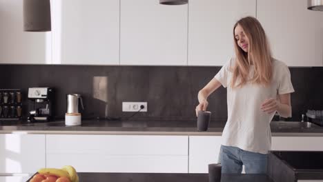 a young woman is dancing in the kitchen and drinking coffee