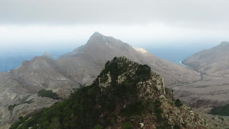 Rocky-peak-on-Porto-Santo-Island-with-low-hanging-clouds,-aerial