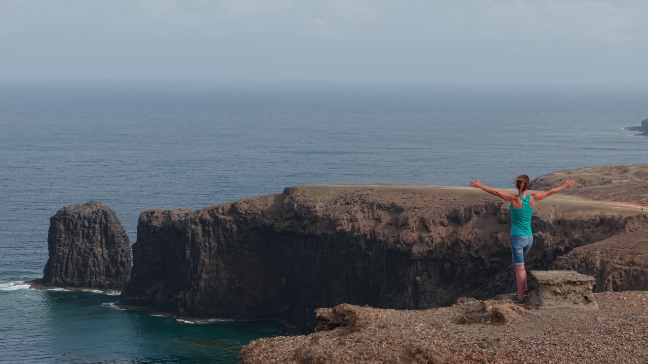 Female tourist spreading arms, experiencing freedom while overlooking dramatic coastal landscape of Gran Canaria with sweeping volcanic terrain and ocean horizon