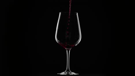 red wine being poured into a glass on a black background with rim lighting, slow motion