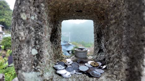 a collection of coins placed on a traditional stone lantern overlooking a scenic japanese background, symbolizing cultural and spiritual practices.