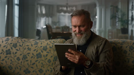 Smiling old man reading news online tablet computer. Happy senior man using pad
