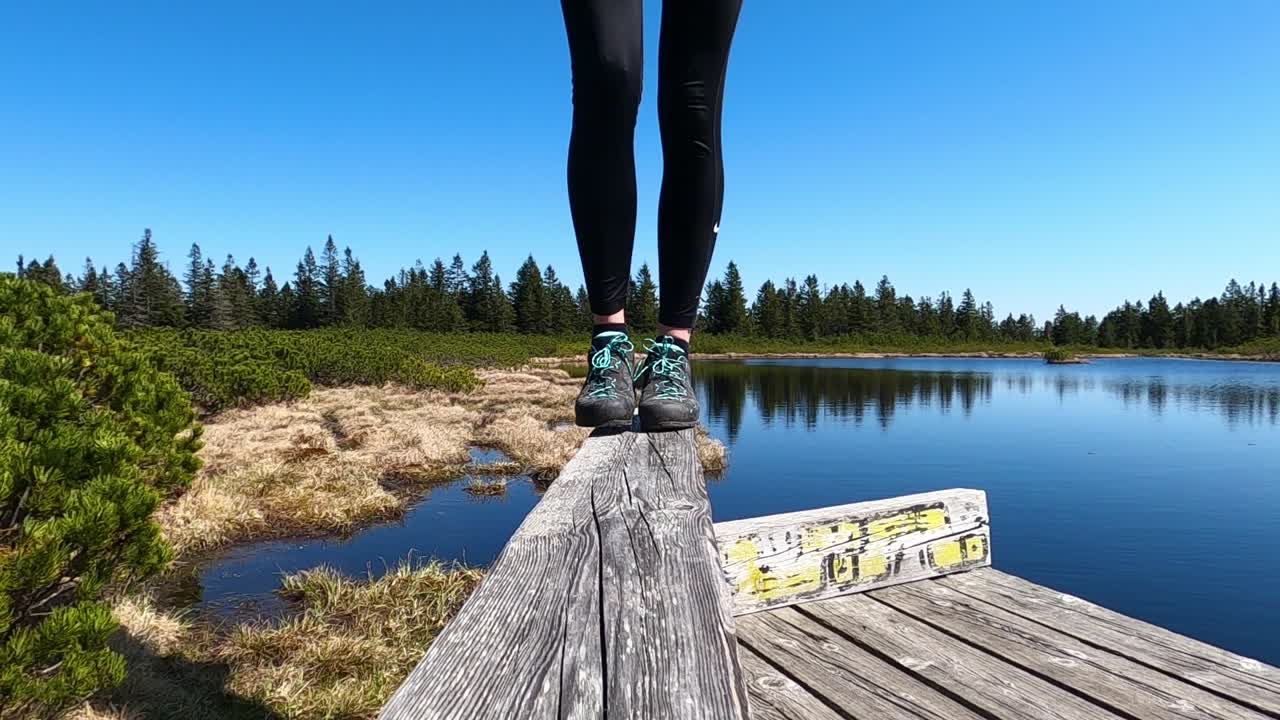 Lower part of woman's legs in low hiking shoes walking on a wooden fence by the lake slow motion