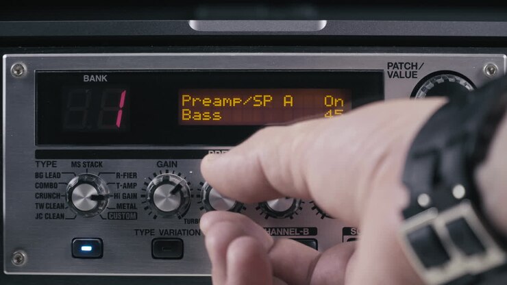 Mani di un musicista impostano i parametri di un preamplificatore per chitarra, primo piano 4K